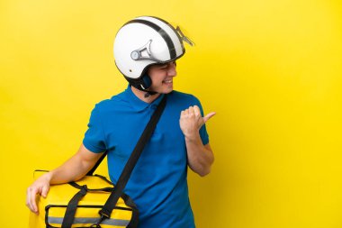 Young Brazilian man with thermal backpack isolated on yellow background pointing to the side to present a product
