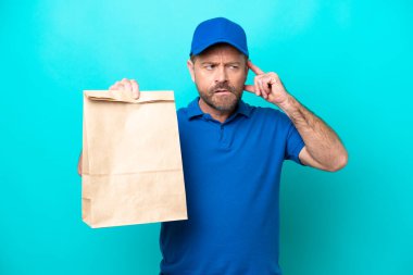 Middle age man taking a bag of takeaway food isolated on blue background having doubts and thinking