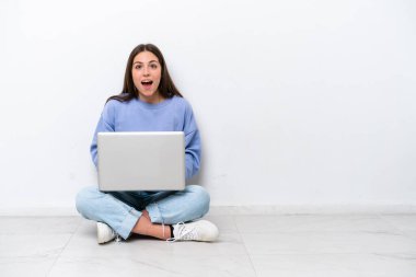 Young caucasian woman with laptop sitting on the floor isolated on white background with surprise facial expression