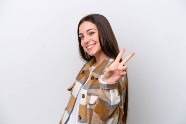 Beyaz arka planda izole edilmiş genç bir kız gülümsüyor ve zafer işareti gösteriyor