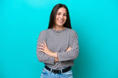 Mavi arka planda izole genç beyaz kadın kollarını ön cephede çapraz tutuyor.