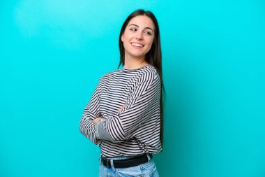 Mavi arka planda izole edilmiş, kolları bağlı ve mutlu genç beyaz bir kadın.