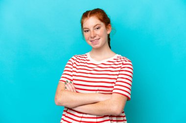 Young reddish woman isolated on blue background keeping the arms crossed in frontal position