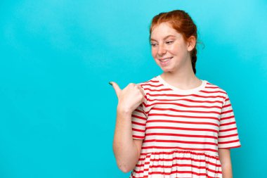 Mavi arka planda izole edilmiş genç bir kadın bir ürünü sunmak için kenarı işaret ediyor.