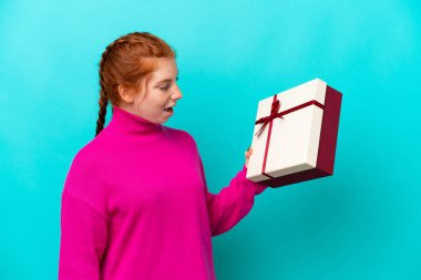 Kafkasyalı genç bir kadın elinde mavi arka planda mutlu bir ifadeyle izole edilmiş bir hediye tutuyor.