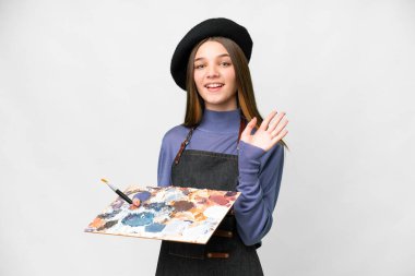 Young artist man holding a palette over isolated white background saluting with hand with happy expression