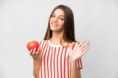 Teenager girl with an apple over isolated white background saluting with hand with happy expression