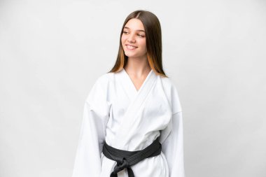 Teenager girl doing karate over isolated white background looking to the side and smiling