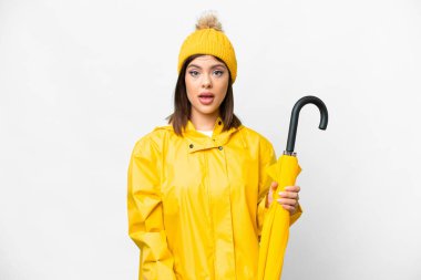 Young Russian woman with rainproof coat and umbrella over isolated white background with surprise facial expression