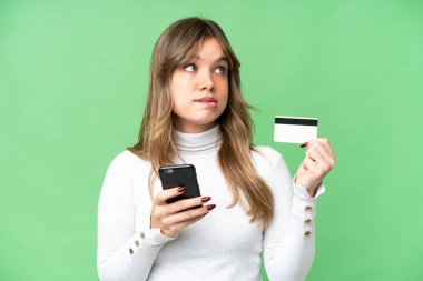 İzole edilmiş krom anahtar geçmişi olan genç bir kız kredi kartıyla cep telefonundan alışveriş yapıyor.