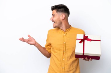 Young caucasian man holding a gift isolated on white background with surprise facial expression