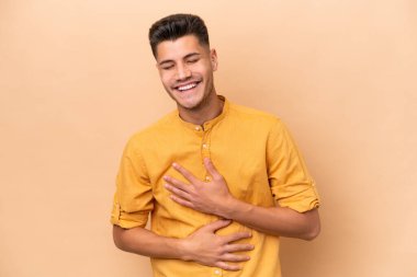 Beyazlı genç bir adam bej arka planda izole edilmiş, çok gülümsüyor.