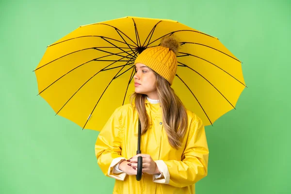 若いです女の子とともにレインプルーフコートと傘上の隔離されたクロマキー背景見ますザサイド — ストック写真