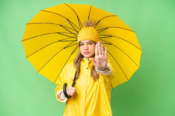 穿着雨衣 披着雨伞的小女孩在孤零零的彩色关键背景上做着停下来的姿势 — 图库照片