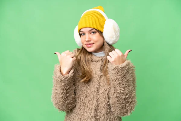 年轻姑娘戴着冬衣 戴在孤立的彩色关键背景上 手指头翘起 微笑着 — 图库照片