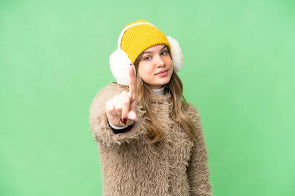 年轻姑娘披着冬衣 戴在孤立的彩色关键背景上 露出并举起一只手指头 — 图库照片