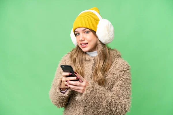 年轻姑娘披着冬衣 罩在孤立的彩色关键背景上 用手机传递信息 — 图库照片