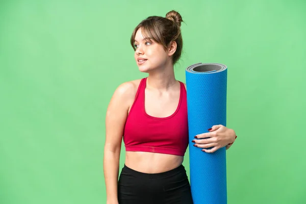 stock image Young sport girl going to yoga classes while holding a mat over isolated chroma key background looking to the side and smiling