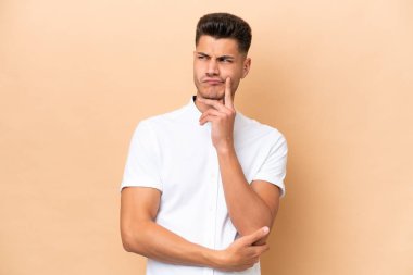 Beyazlı genç bir adam bej arka planda izole edilmiş. Şüpheleri ve düşünceleri var.