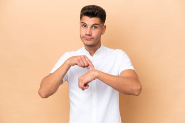 Beyazlı genç bir adam bej arka planda izole edilmiş. Geç kalma jesti yapıyor.