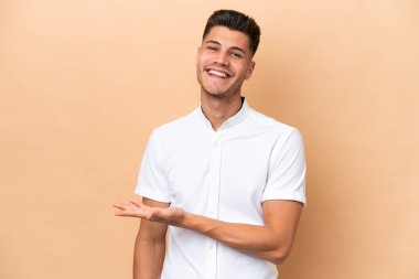 Beyazlı genç bir adam bej arka planda izole edilmiş bir şekilde gülümserken bir fikir sunuyor.