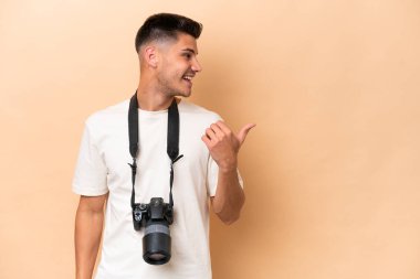 Genç fotoğrafçı, bej arka planda izole edilmiş beyaz bir adam bir ürünü sunmak için kenarı işaret ediyor.