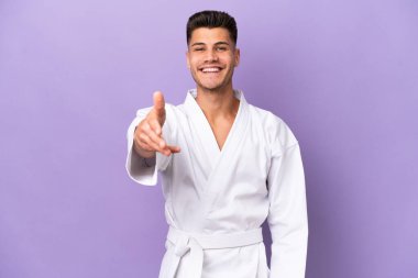 Mor arka planda karate yapan genç beyaz adam iyi bir anlaşma için el sıkışıyor.