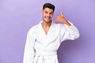 Mor arka planda karate yapan genç beyaz bir adam telefon jesti yapıyor. Bana geri dönüş işareti ver.