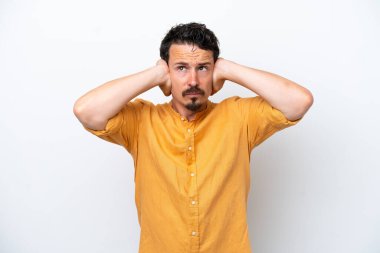 Bıyıklı genç adam beyaz arka planda izole edilmiş hayal kırıklığına uğramış ve kulaklarını kapatmış.