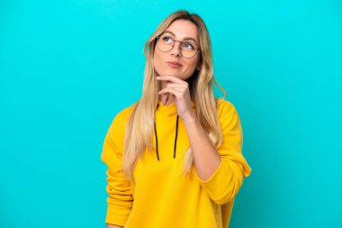 Genç Uruguaylı kadın mavi arka planda izole edilmiş gülümserken yukarı bakıyor