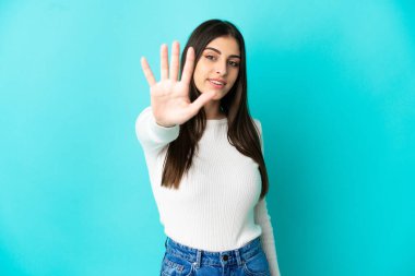 Mavi arka planda izole edilmiş genç beyaz kadın parmaklarıyla beşi sayıyor.