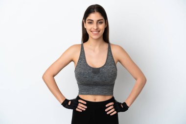 Beyaz arka planda izole edilmiş genç beyaz kadın kolları kalçasında ve gülümsüyor.