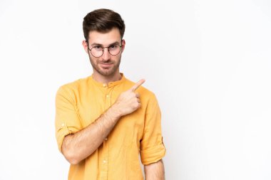 Beyaz arka planda izole edilmiş genç beyaz bir adam bir ürün sunmak için kenarı işaret ediyor.