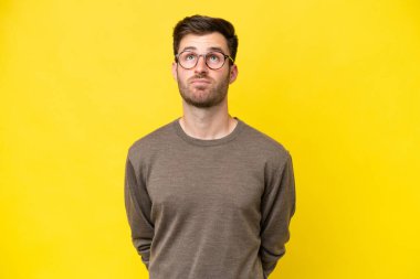 Genç beyaz adam sarı arka planda izole edilmiş ve yukarı bakıyor.