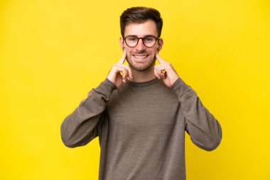 Sarı arka planda izole edilmiş genç beyaz adam mutlu ve hoş bir ifadeyle gülümsüyor.