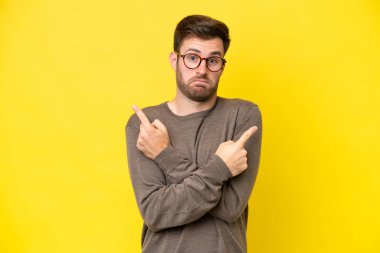 Sarı arka planda izole edilmiş genç beyaz adam, yan taraftakilerin şüphelerine işaret ediyor.