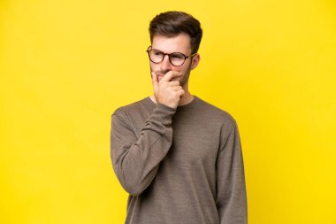 Sarı arka planda izole edilmiş genç beyaz adamın şüpheleri ve şaşkın bir yüz ifadesi var.