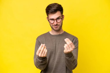 Sarı arka planda izole genç beyaz adam para hareketi yapıyor.