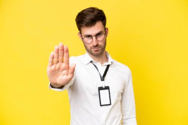 Young caucasian with ID card isolated on yellow background making stop gesture