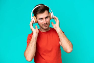 Genç beyaz adam mavi arka planda izole edilmiş müzik dinliyor.