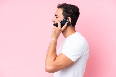 Pembe arka planda izole edilmiş genç beyaz bir adam cep telefonuyla sohbet ediyor.