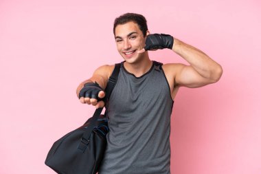 Young sport caucasian man with sport bag isolated on pink background making phone gesture and pointing front
