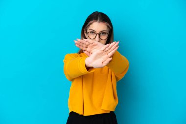 Kafkasyalı genç bir kadın, mavi arka planda izole edilmiş bir şekilde bir eylemi durdurmak için el hareketi yapıyor.