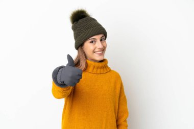 Kış şapkalı genç kız beyaz arka planda izole edildi. Başparmakları havada çünkü iyi bir şey oldu.