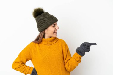 Kışlık şapkalı genç bir kız beyaz arka planda izole edilmiş bir şekilde parmak ucunda bir ürün sunuyor.