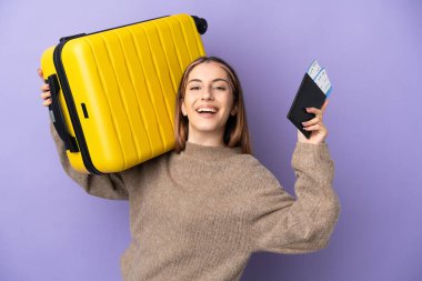 Mor arka planda izole edilmiş genç beyaz bir kadın, bavul ve pasaportla tatilde.