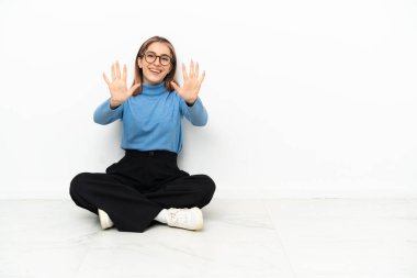 Young Caucasian woman sitting on the floor counting ten with fingers
