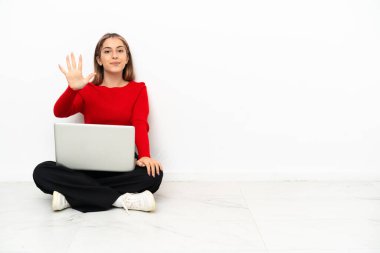 Young caucasian woman with a laptop sitting on the floor counting five with fingers