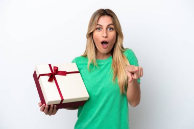 Young Uruguayan woman holding a gift isolated on white background surprised and pointing front