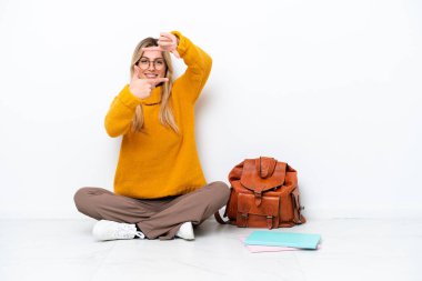Uruguayan student woman sitting one the floor isolated on white background focusing face. Framing symbol